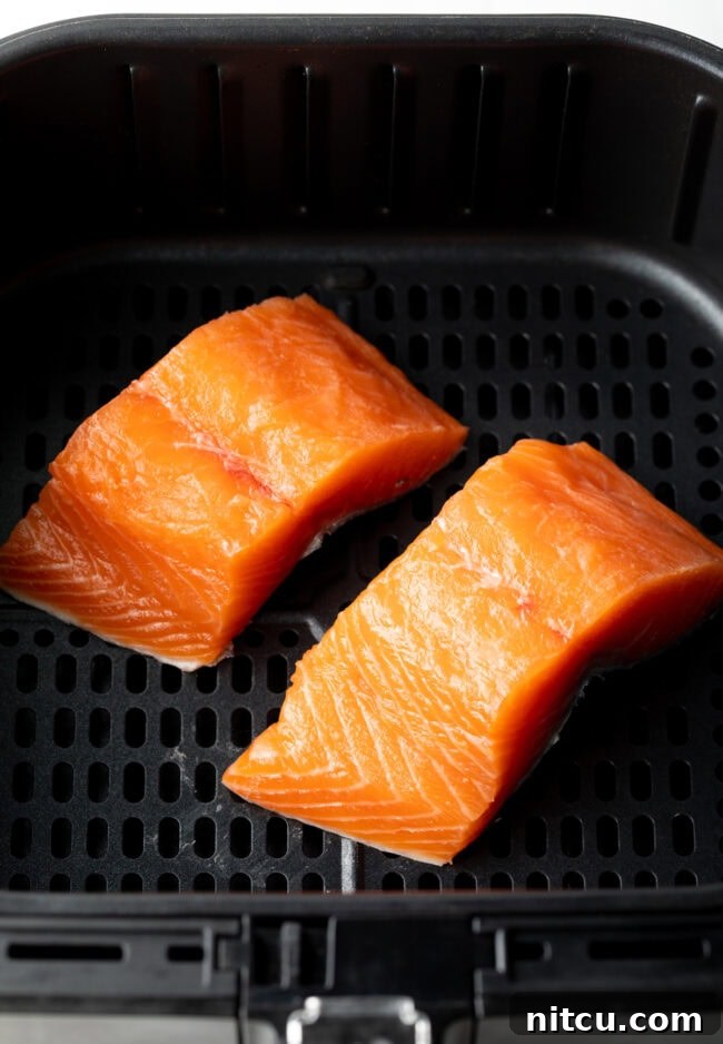 Two uncooked salmon fillets in the air fryer, ready for cooking.