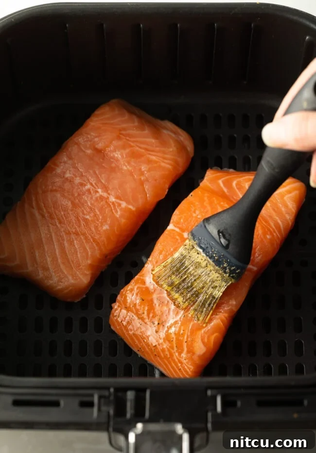 Hand brushing seasonings over uncooked salmon fillets in the air fryer.