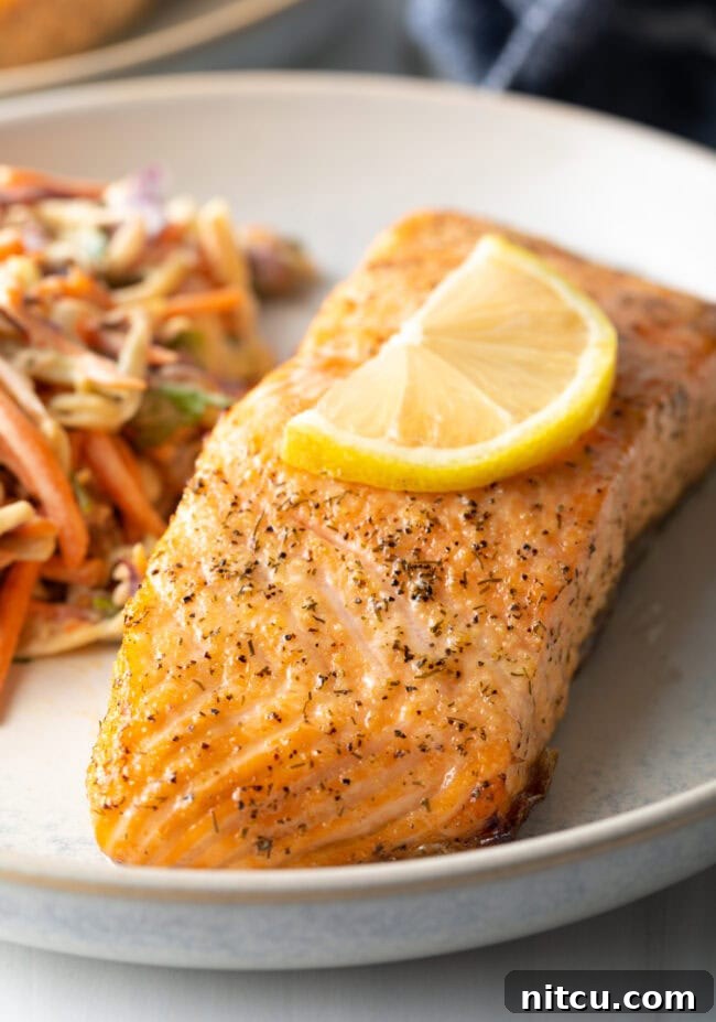 Close view cooked salmon fillet on a plate with garnish of lemon slice, coleslaw side.