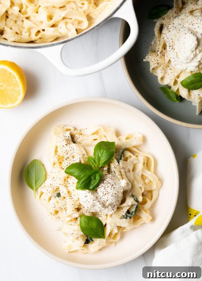 Top down view of a bowl of creamy lemon ricotta pasta with a pot of cooking pasta in the background.