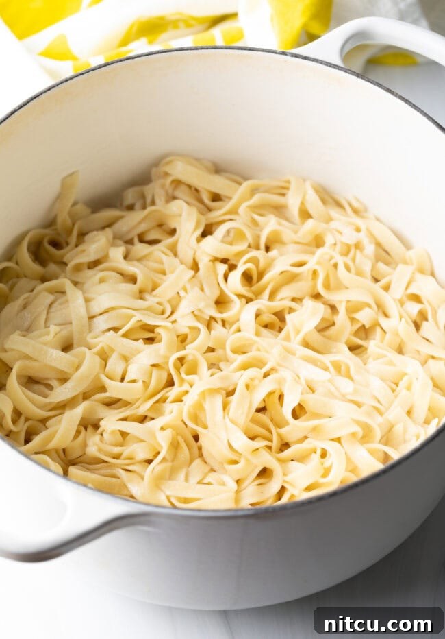 Large pot of cooked fettuccine noodles in a creamy sauce.