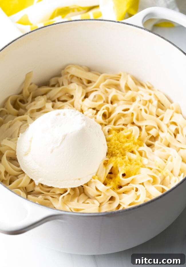 Pot with fettuccine, garlic and lemon, and large scoop of ricotta cheese on top, ready to be stirred.