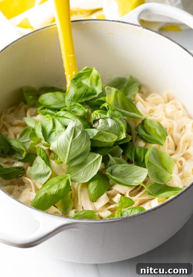 Stirring fresh basil into the pot of pasta, completing the dish.