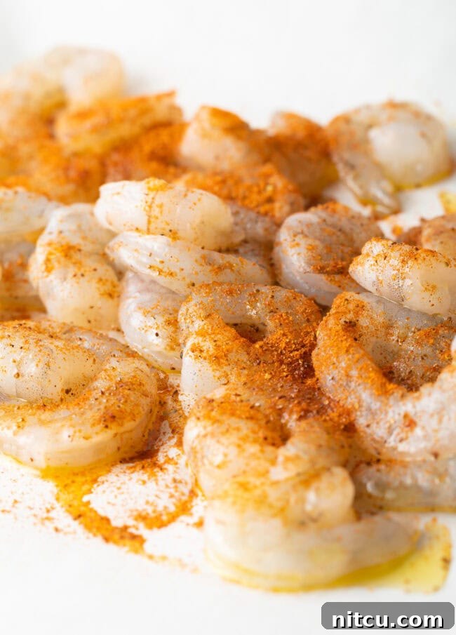 Raw shrimp uniformly tossed with vibrant Cajun seasonings in a mixing bowl, ready for roasting.