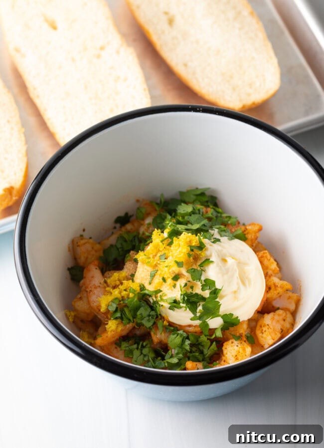 A mixing bowl containing cooked, chopped shrimp, creamy mayonnaise, vibrant lemon zest, and fresh parsley, ready to be combined.