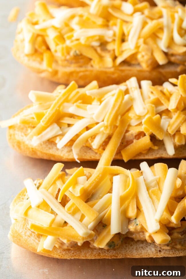 Shredded cheese generously sprinkled over the baguette pieces topped with the shrimp mixture, preparing for the final bake.