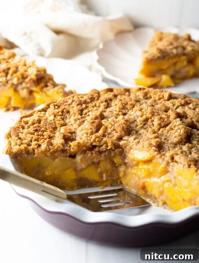 A golden-brown peach crumble pie, freshly baked, with a spatula ready to serve a slice.