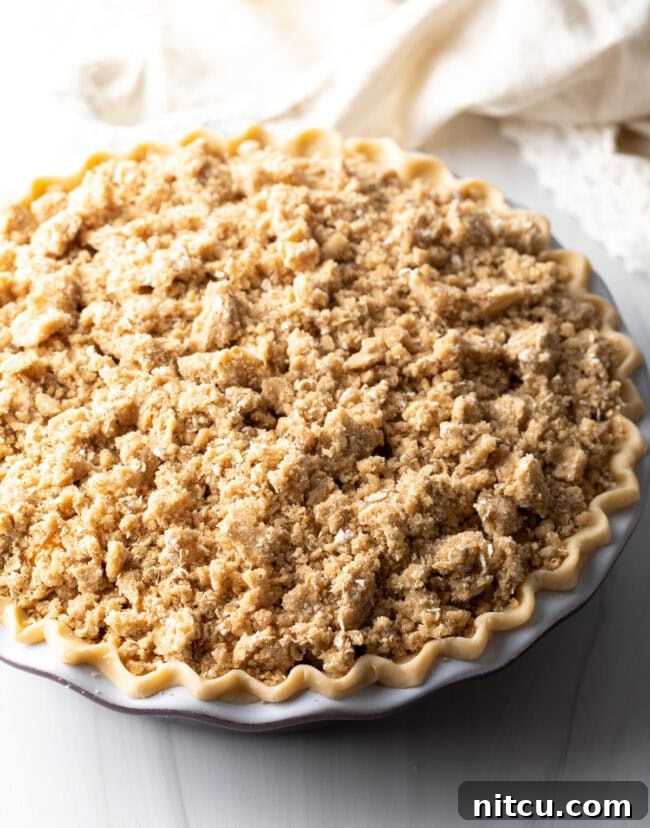 Sprinkling the oat crumble evenly over the peach filling in the pie crust.