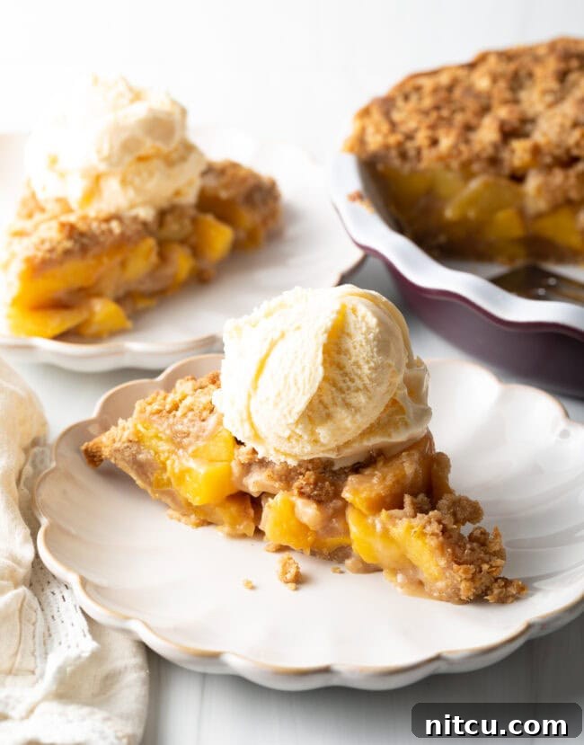 A delectable piece of peach crumble pie with a scoop of ice cream on top, ready to be enjoyed.