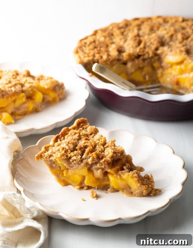 A single slice of freshly baked peach crumble pie on a white plate, showcasing its golden crust and juicy peach filling.