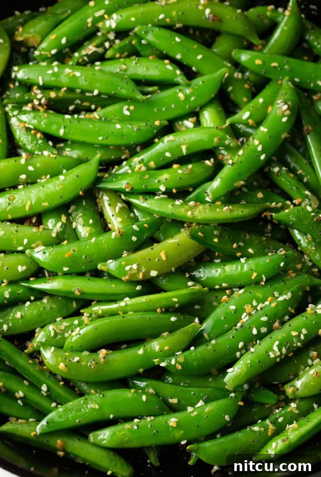 Close-up shot of sesame garlic stir-fried snap peas in a large skillet, highlighting the fresh texture and seasoning.