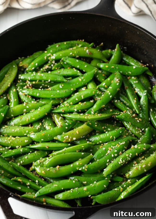 Final close-up shot of the stir-fried sugar snap peas in a white serving bowl, garnished with extra sesame seeds.