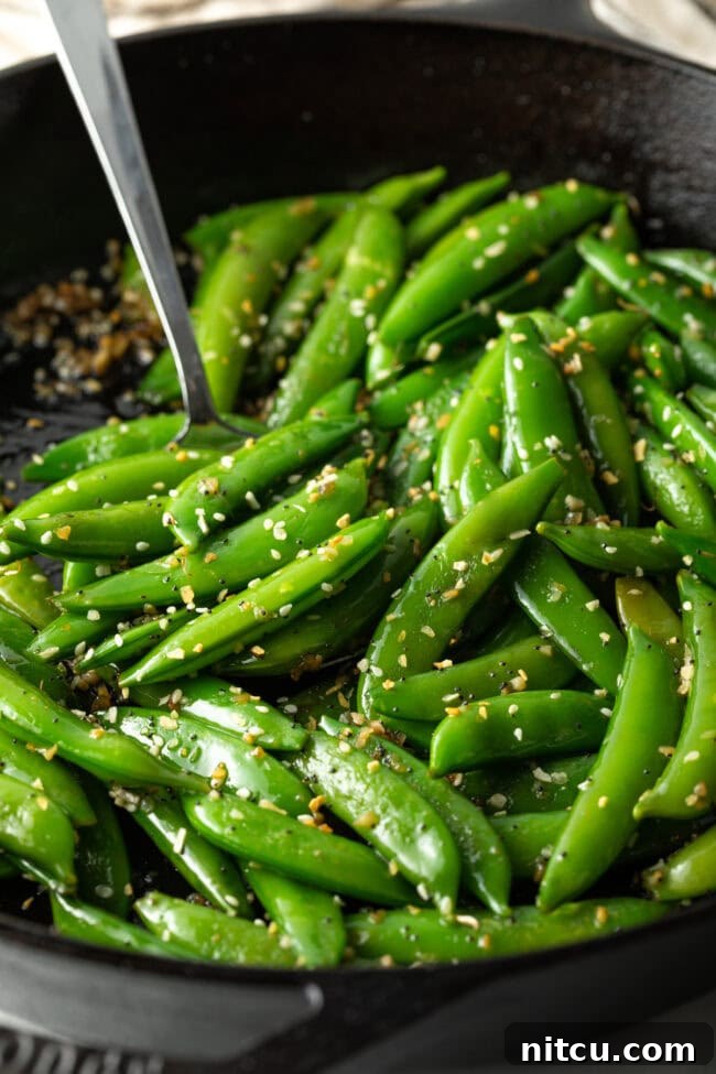 Close-up final serving of vibrant green sugar snap peas, perfectly cooked and seasoned, in a rustic bowl.