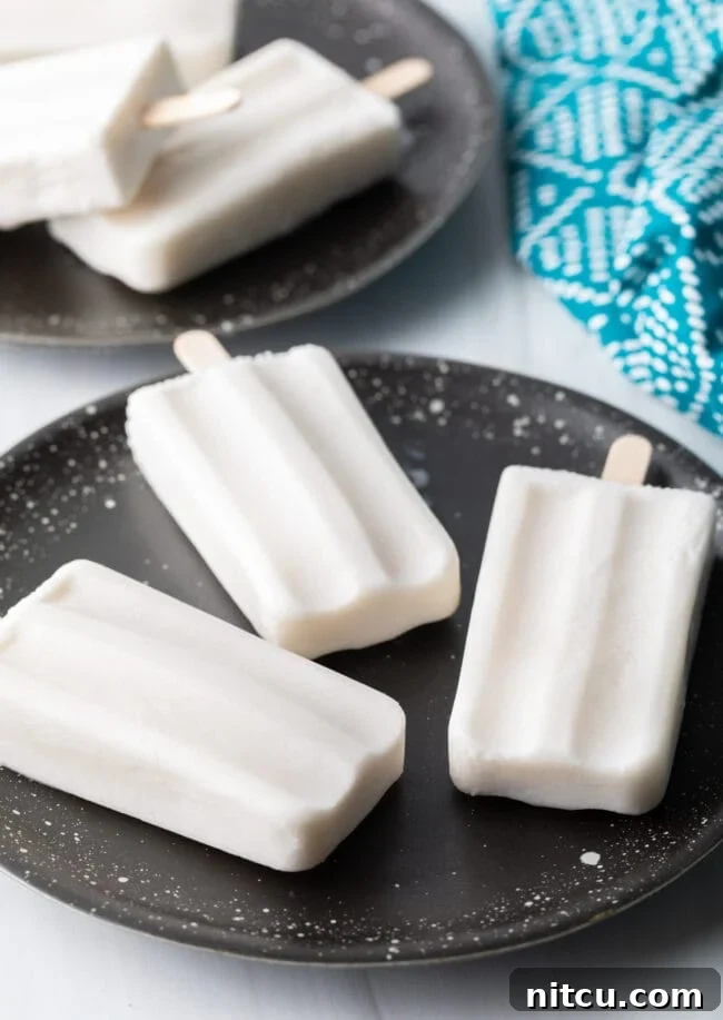 Three perfectly frozen coconut milk popsicles arranged on a rustic plate, ready to be enjoyed.
