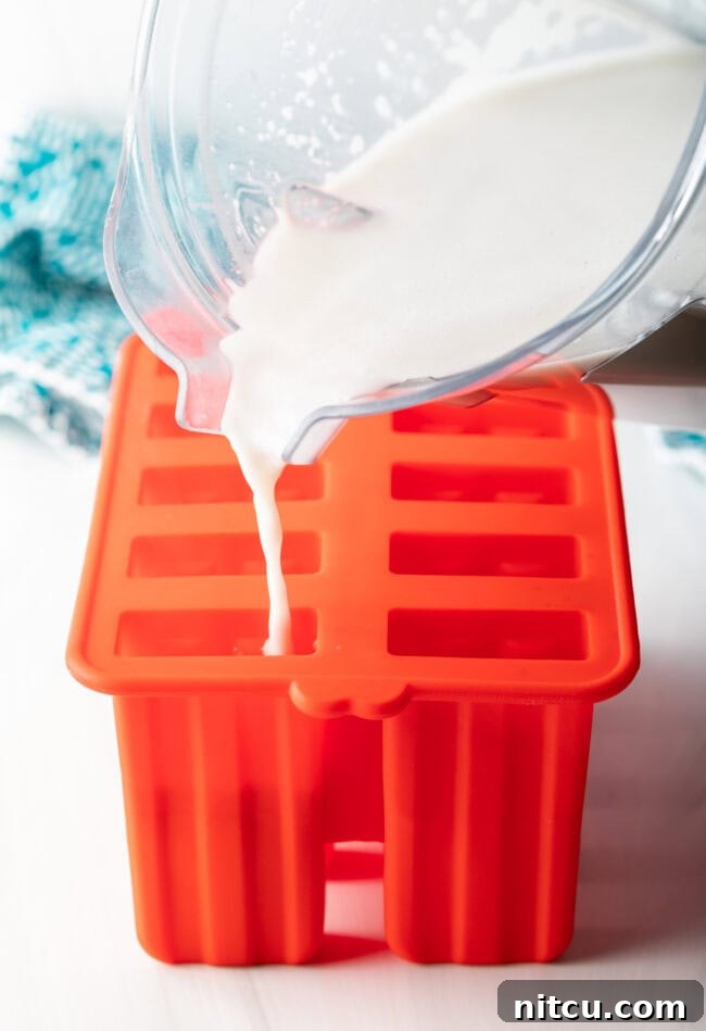 The creamy coconut milk mixture being poured into individual compartments of a popsicle mold.