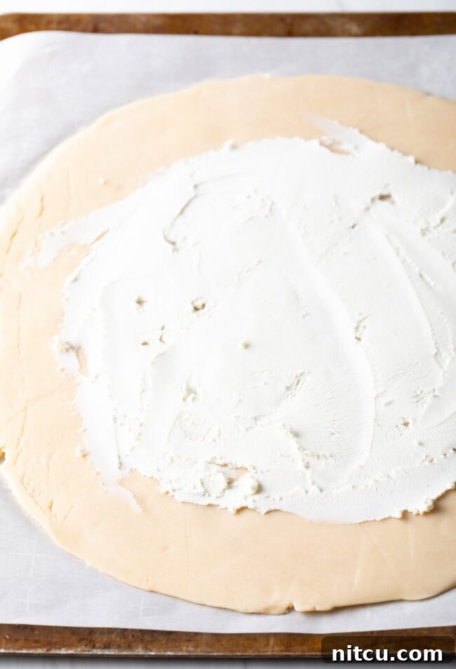 Step-by-step image of softened goat cheese being spread evenly over the pie crust, leaving a rim.