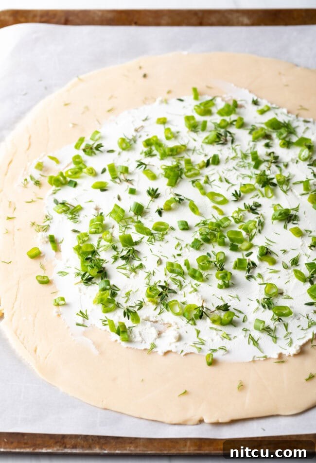 Step-by-step image of chopped scallions, thyme, and dill sprinkled over the goat cheese layer.