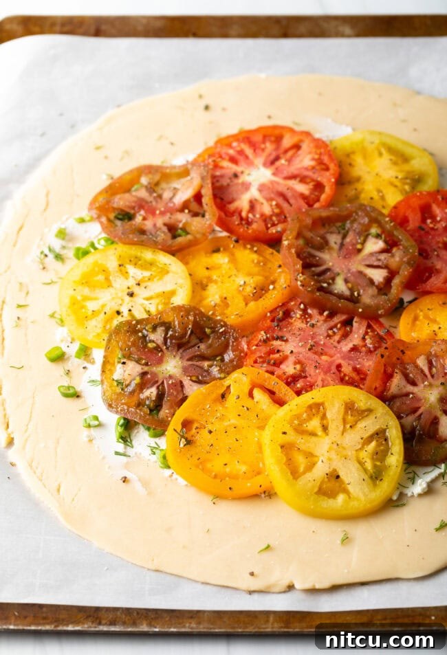 Step-by-step image of sliced heirloom tomatoes being carefully arranged and overlapped on top of the herb and goat cheese layer.