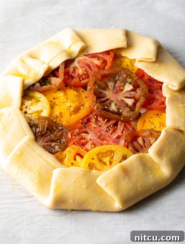 Step-by-step image showing the edge of the pie crust being folded over the tomatoes to create a rustic crimped border.
