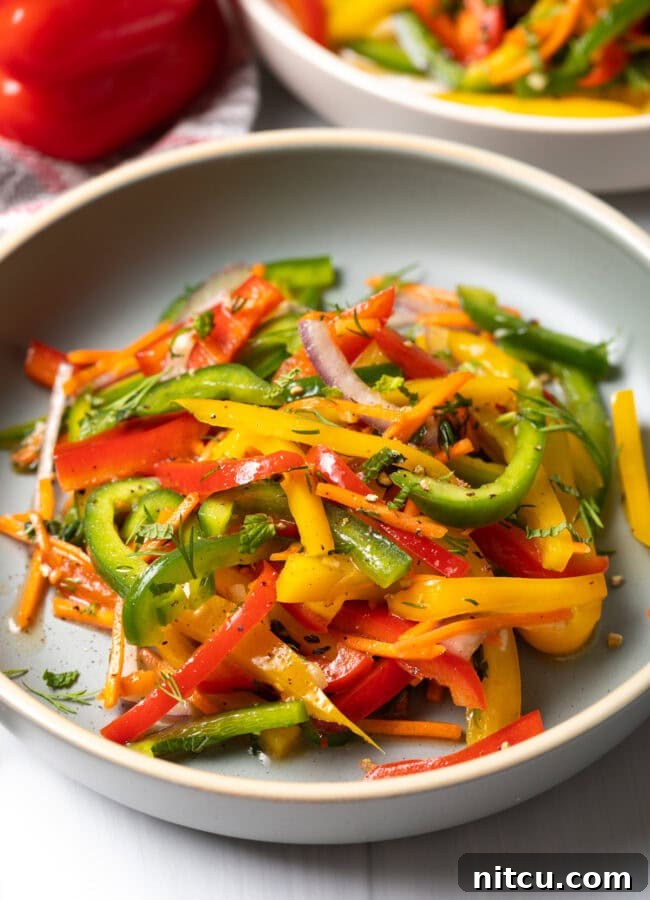 A vibrant summer bell pepper salad featuring yellow, green, and red peppers, served in a stylish white plate.
