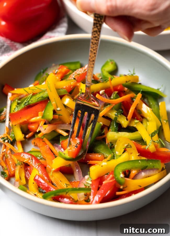 A fork taking a delicious bite of the bell pepper salad from a bowl, showcasing its freshness.