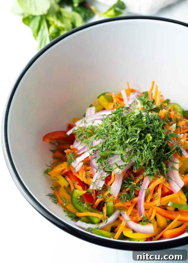 Freshly chopped dill and mint added to the bowl of sliced vegetables for the bell pepper salad, enhancing its aromatic appeal.