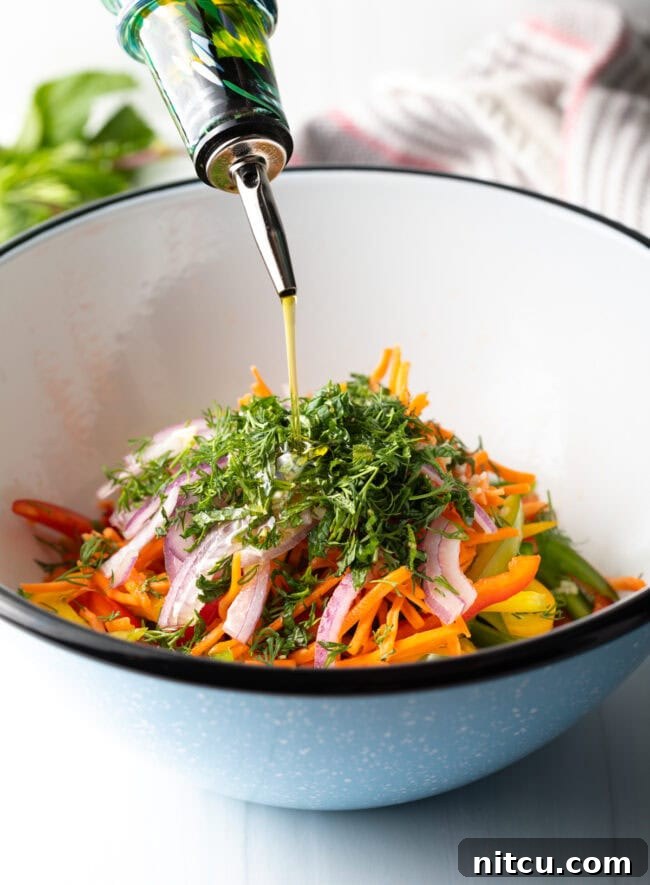 A close-up shot of olive oil being drizzled over the colorful bell pepper ingredients in a bowl, just before tossing.