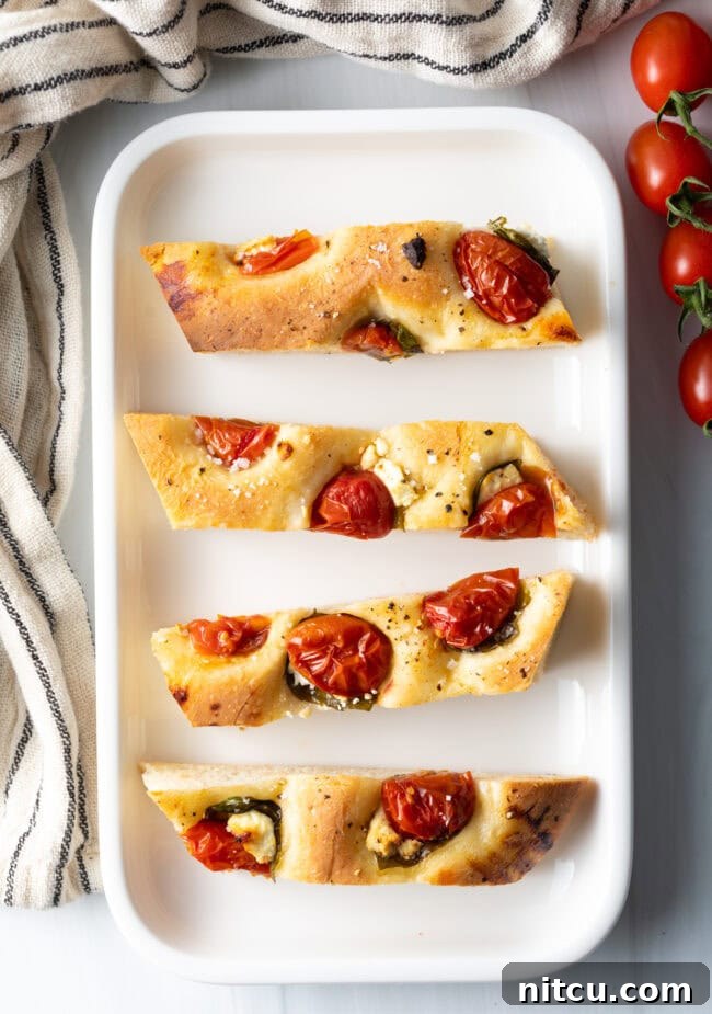 Top down view 4 pieces of tomato basil focaccia bread on a white platter.