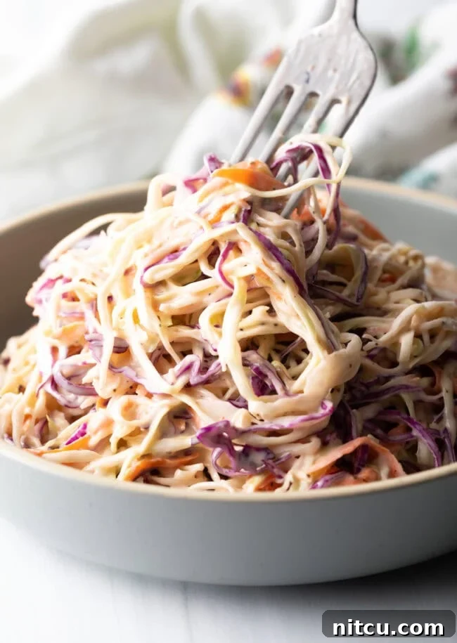 A fork taking a bite from a mound of creamy Southern coleslaw, ready to be enjoyed.
