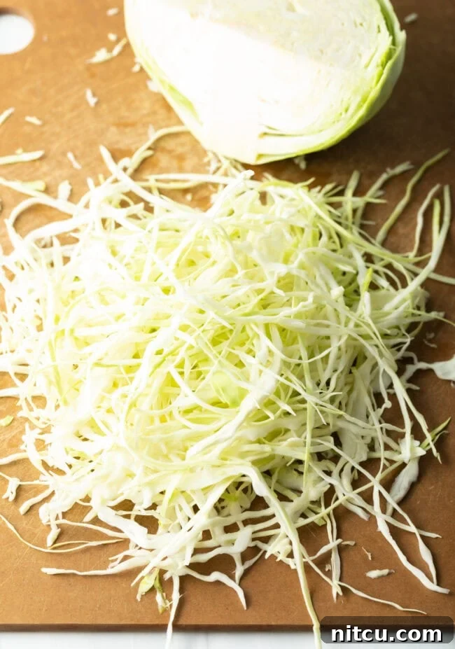 Freshly shredded green cabbage resting on a wooden cutting board, ready for the coleslaw mix.
