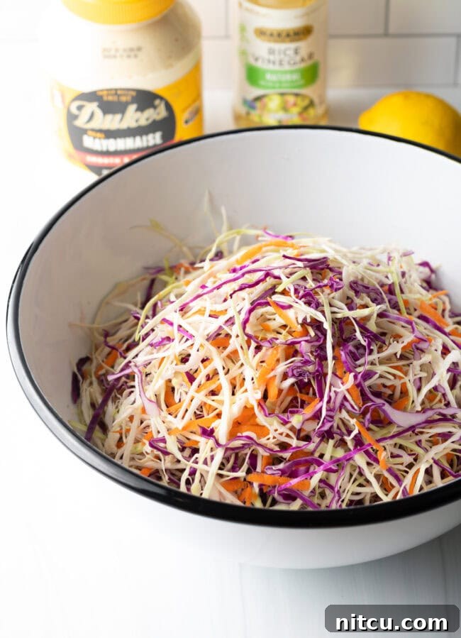 Shredded green and red cabbage along with carrots expertly tossed together in a large bowl.