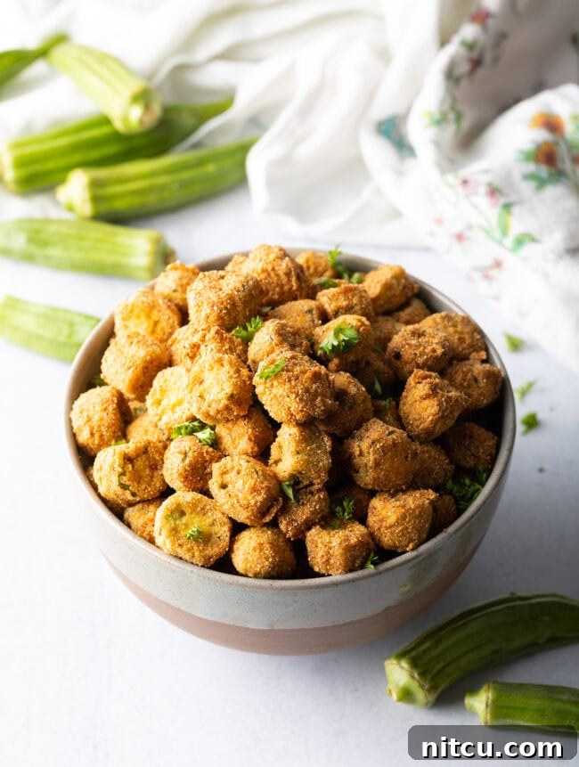 Top down view of a ceramic bowl filled with freshly fried okra pieces, highlighting their golden brown coating and inviting texture.
