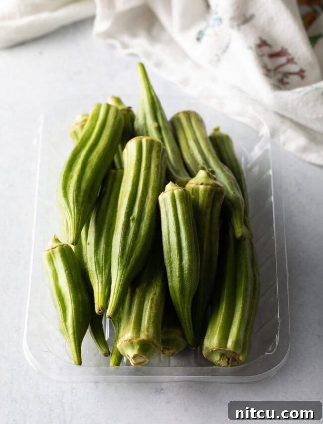 Raw, whole okra pods displayed in a clear plastic container, showing their fresh, vibrant green color and readiness for preparation.