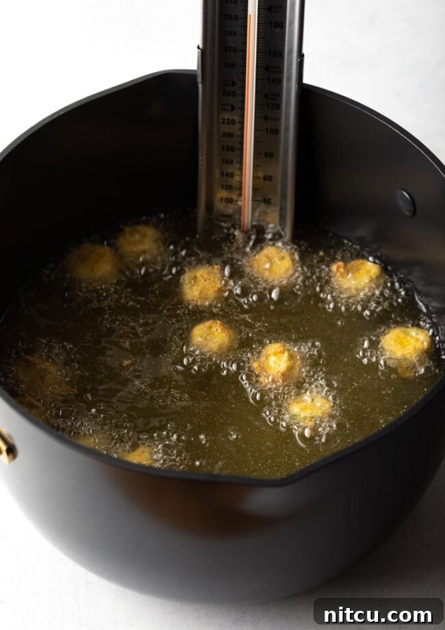 Breaded okra pieces sizzling and frying in hot oil within a large pot, turning golden brown.