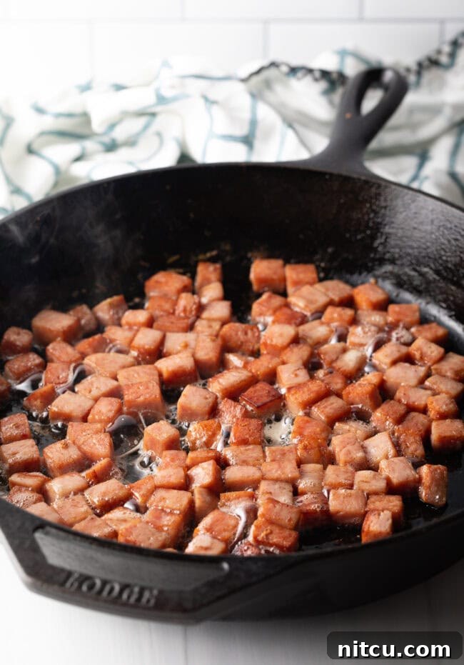 Frying cubes of spam in a cast iron skillet.