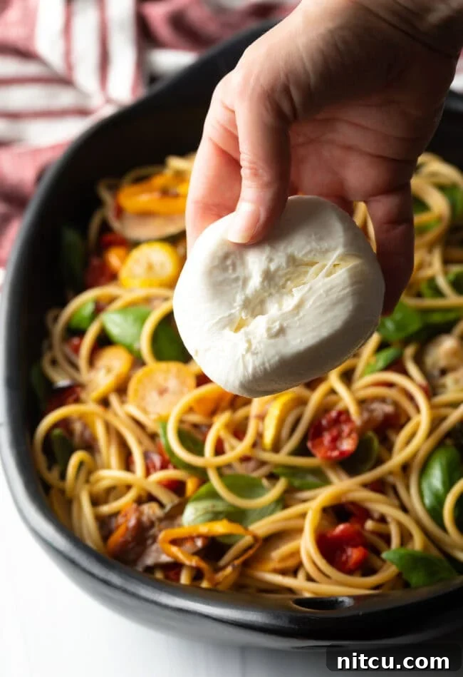 Hand adding a ball of burrata cheese, split in half, to the finished pasta dish.