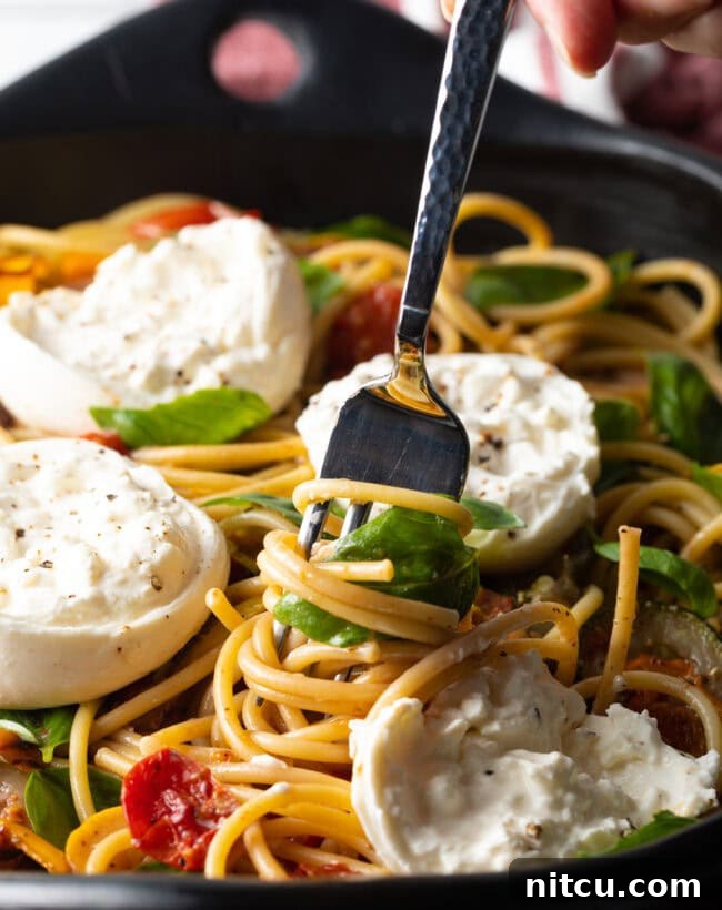 Close-up view of a fork twisting pasta with burrata and roasted vegetables.