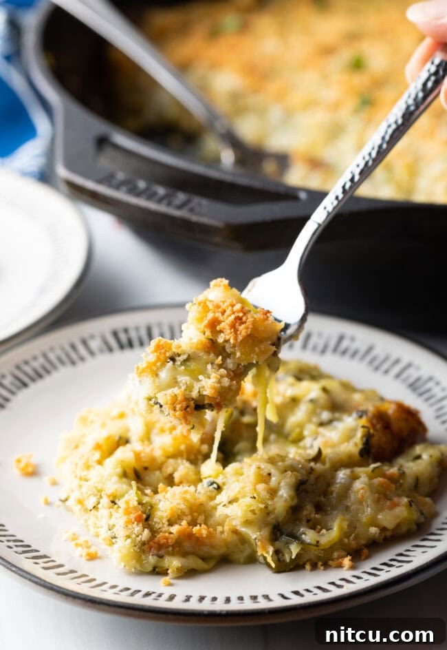 Fork holding bite of cheesy zucchini casserole from the plate to camera.