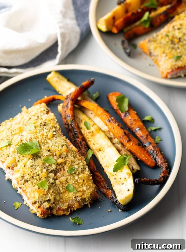 Top down view of baked pesto salmon with panko, grilled veggies on the side.