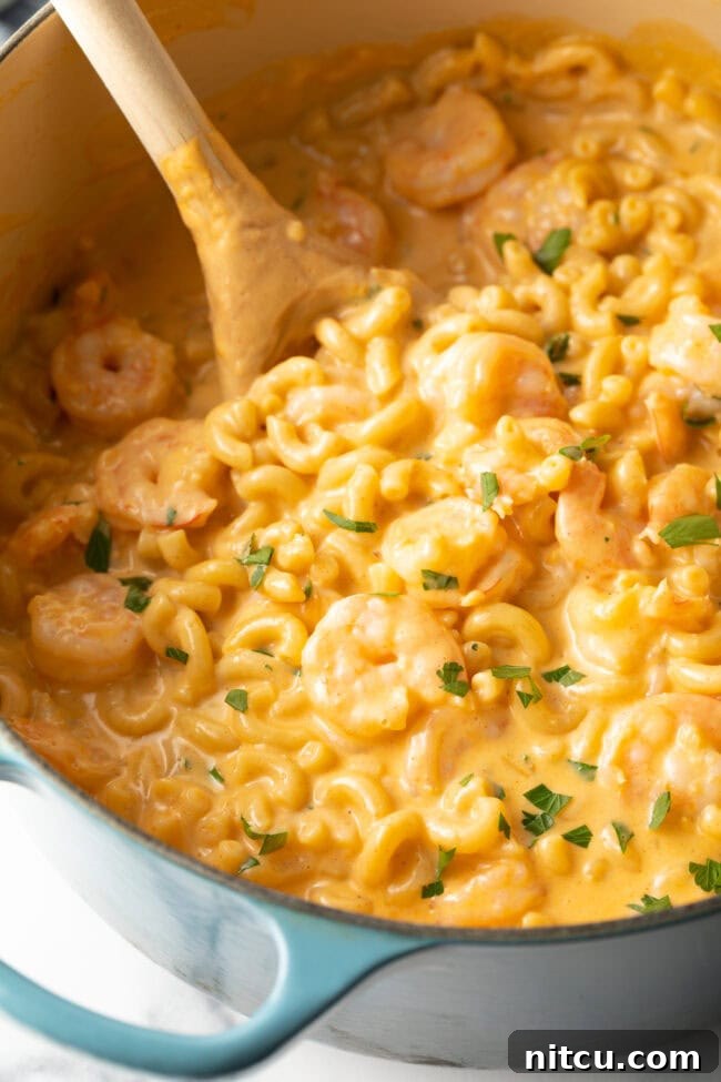 Closeup view of a pot of creamy macaroni and cheese with shrimp, generously sprinkled with fresh chopped parsley.