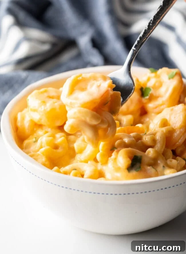 Bowl with a generous serving of shrimp mac & cheese, a fork taking a bite from the bowl, showing the creamy texture.
