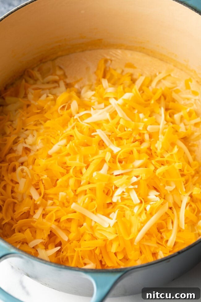 Freshly shredded cheese being added to the pot with the creamy sauce base.