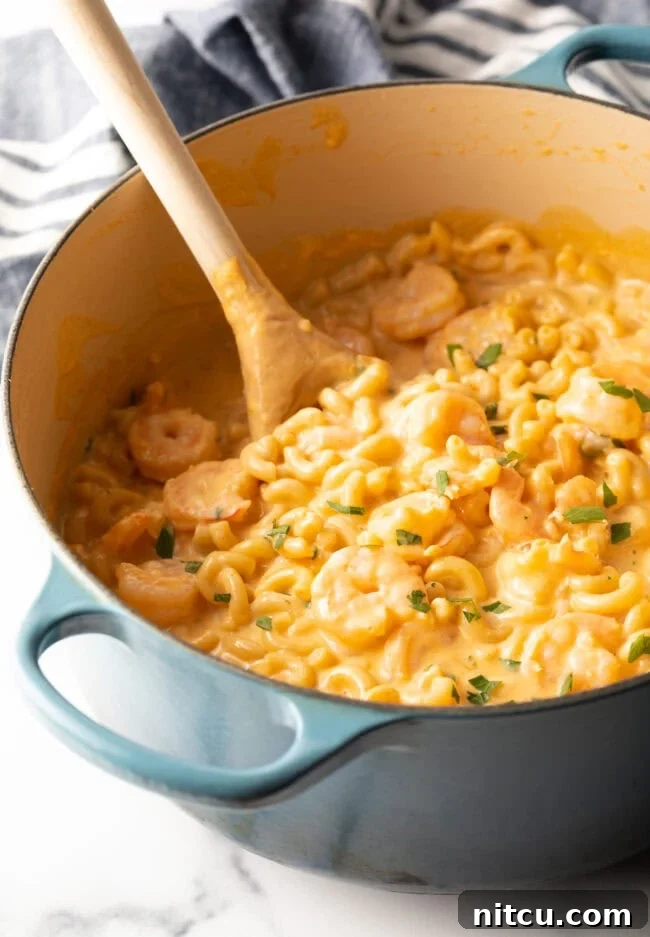 Top down view of a cooking pot with a wooden spoon and the finished, creamy shrimp mac and cheese dish.