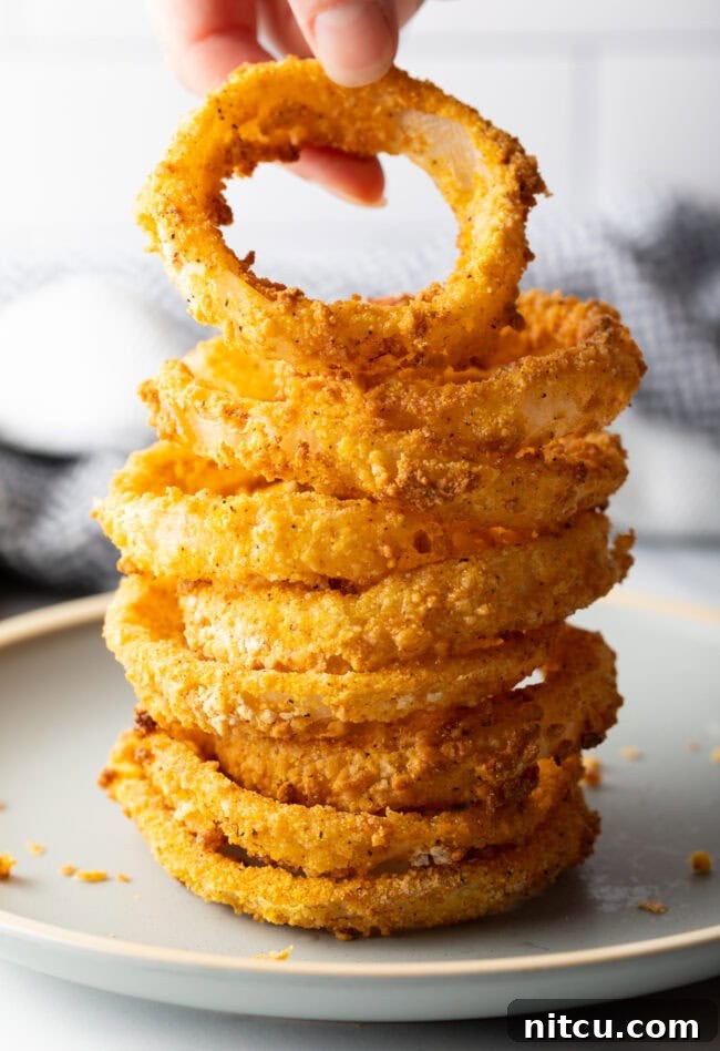 Hand adding onion ring to stack of air fried rings.
