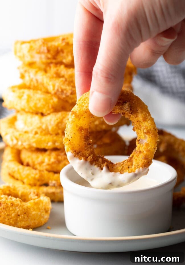 Hand dipping air fryer onion ring into sauce.