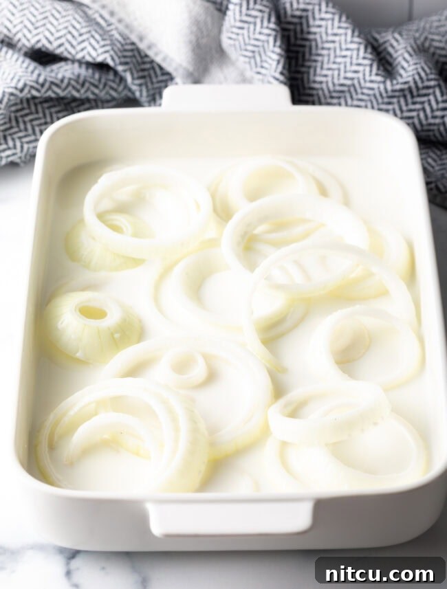 Onion rings in a baking dish soaked in buttermilk.