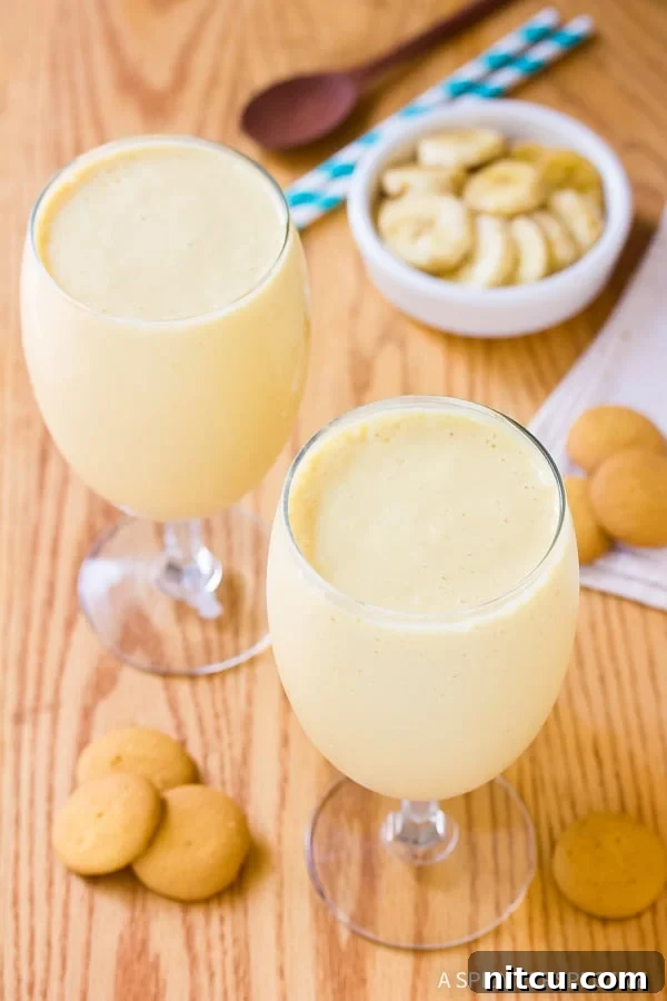 A tall glass of Banana Pudding Milkshake garnished with whipped cream and cookies