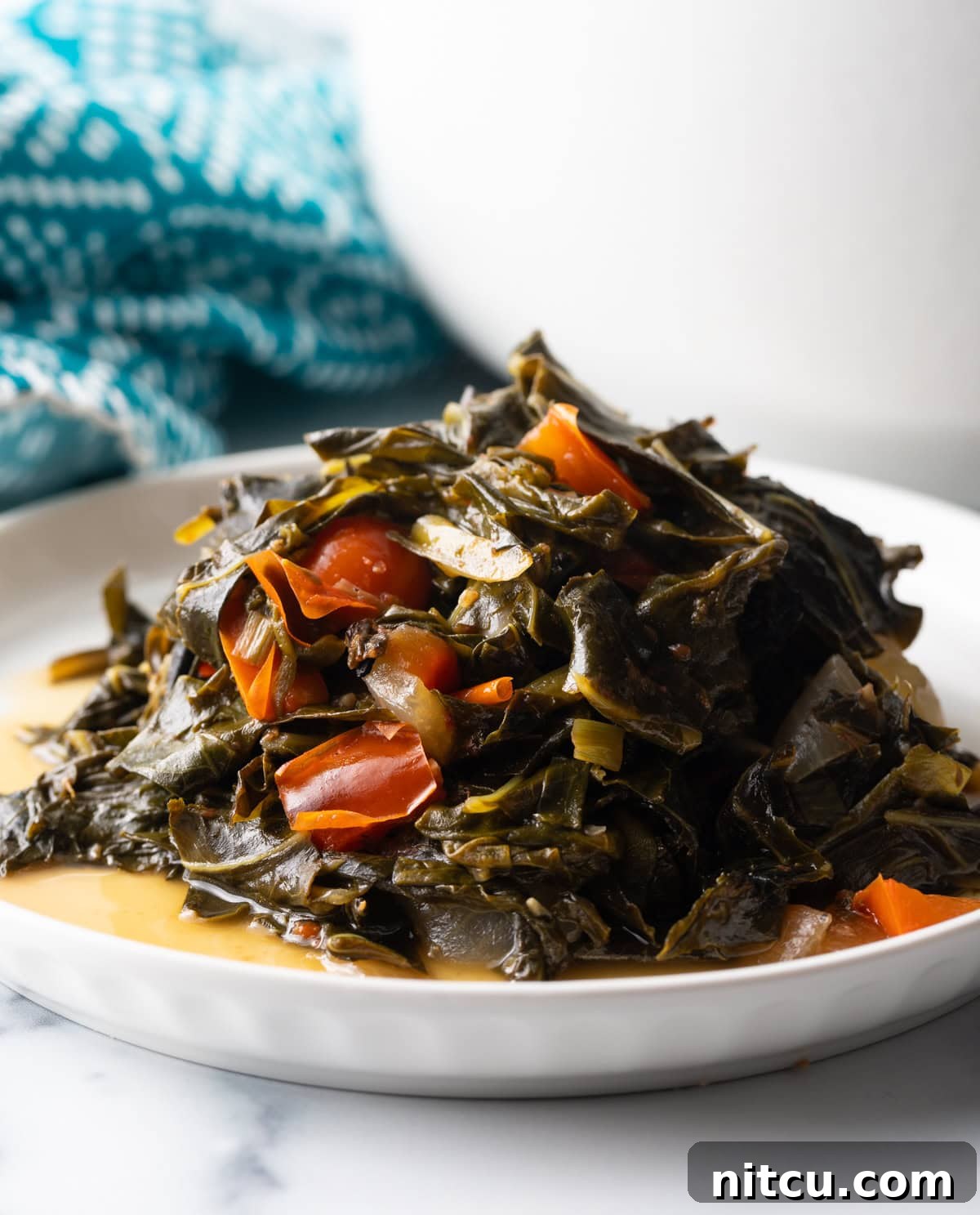 Close side view, small mound of Jamaican collard greens on a white plate. A hearty serving of Jamaican Callaloo, showcasing its rich, stewed texture and vibrant green color, perfectly portioned on a crisp white plate.