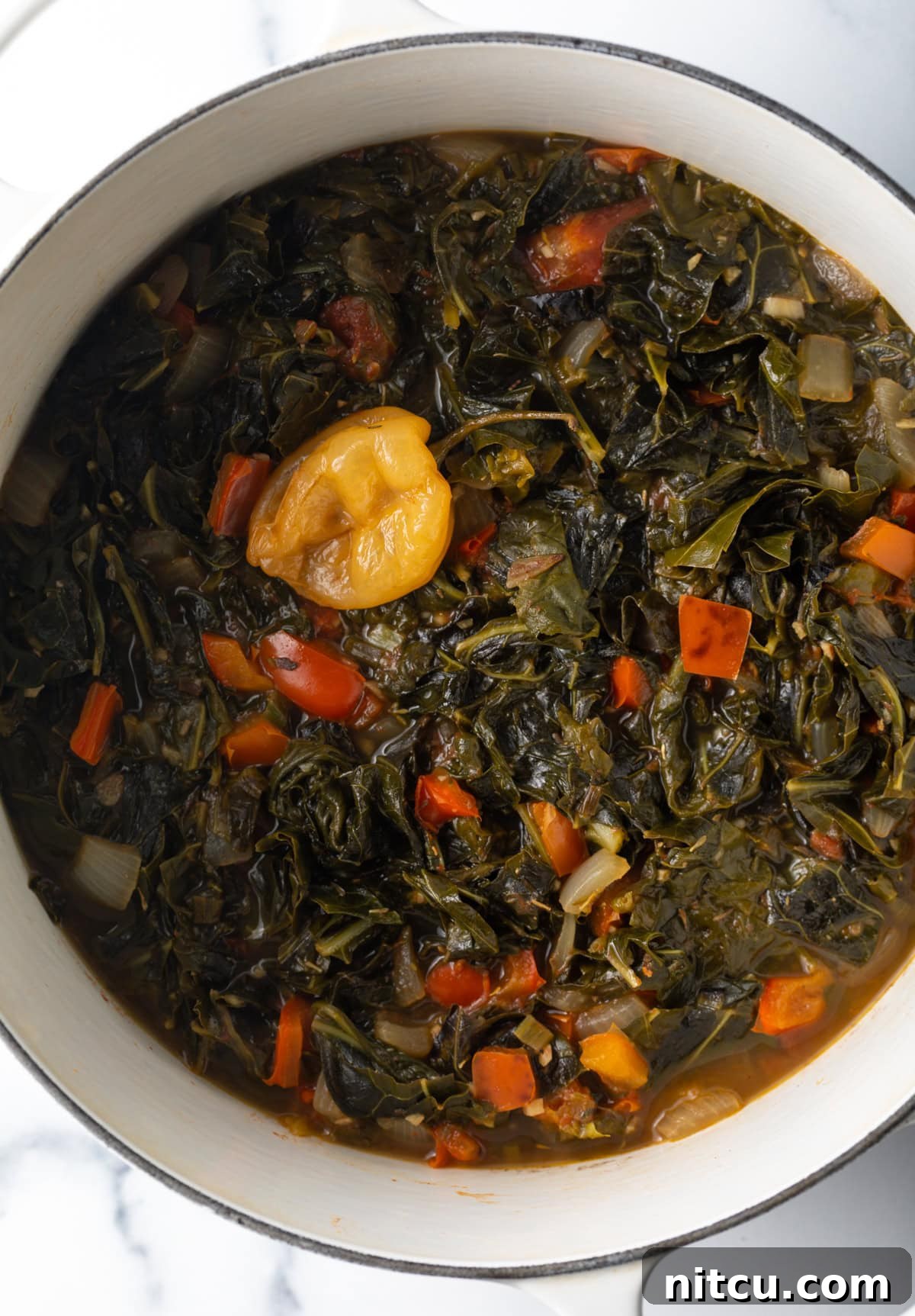 Caribbean stewed greens in large white pot. A large white pot filled with simmering Caribbean stewed greens, showing the rich, vibrant mix of vegetables slowly cooking to perfection.