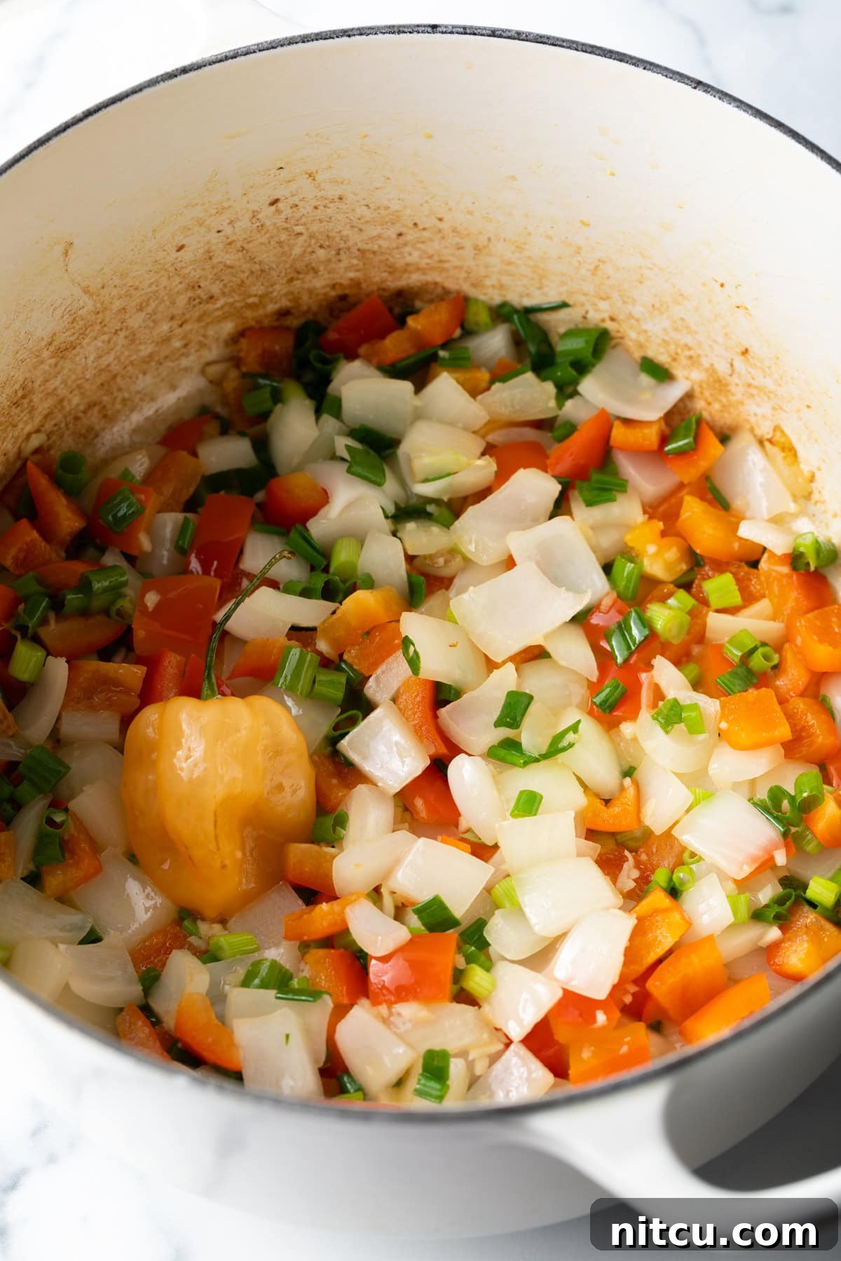 Chopped onions, red bell peppers and veggies sauteeing in a pot. A close-up shot of chopped onions, red bell peppers, and other vibrant vegetables gently sautéing in a large pot, forming the aromatic base of the dish.